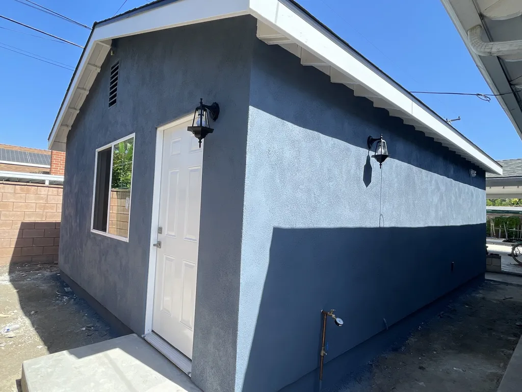 Finished detached accessory dwelling unit with stucco walls, entry door and two exterior lights