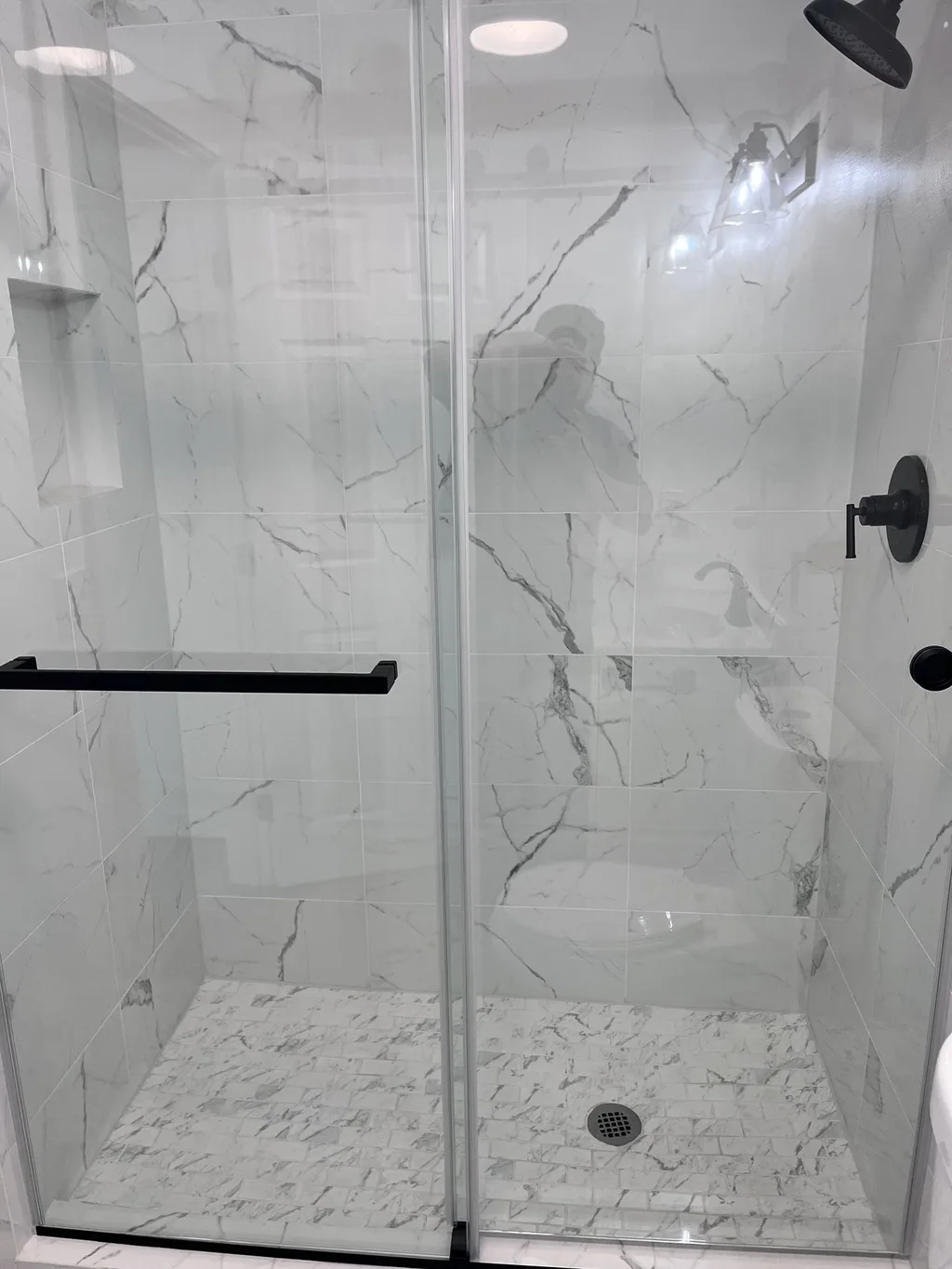 Finished walk-in shower with glass doors, tiled walls, a corner niche and dark fixtures