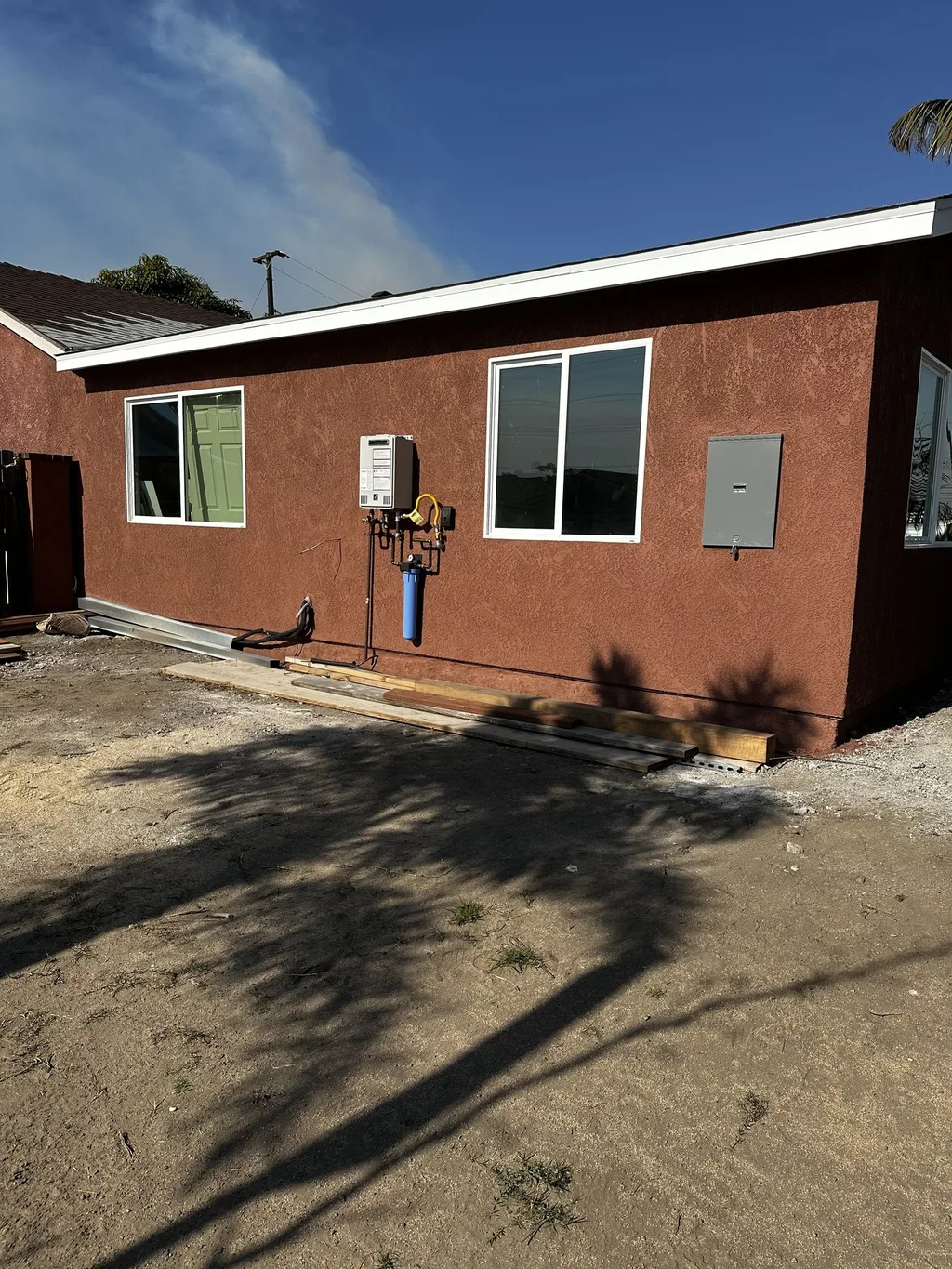 Rear wall of a house with new stucco, white-framed windows and exterior utility connections